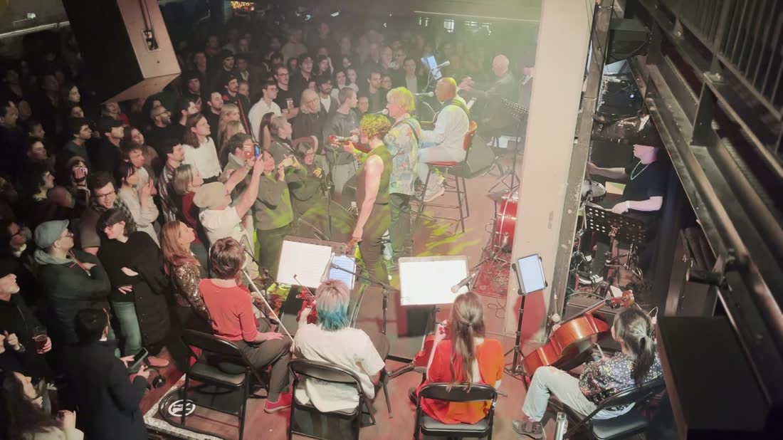 A full room in London watching Gui Tavares perform, with a string section seated in front of the stage
