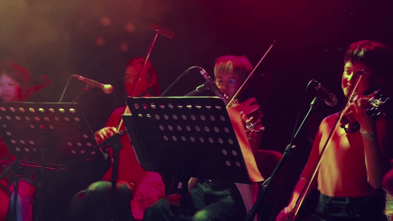 String section on stage under red and amber light at a Gui Tavares concert in London