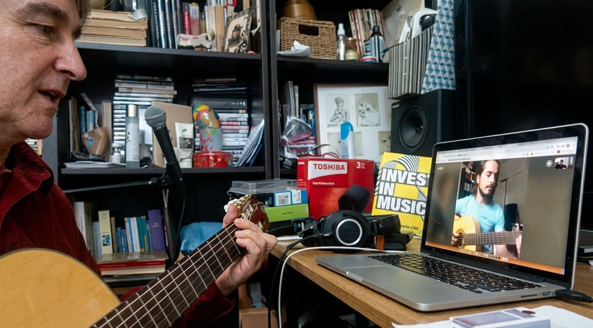 Gui Tavares playing nylon string guitar in front of a laptop, teaching a student who is playing along on screen