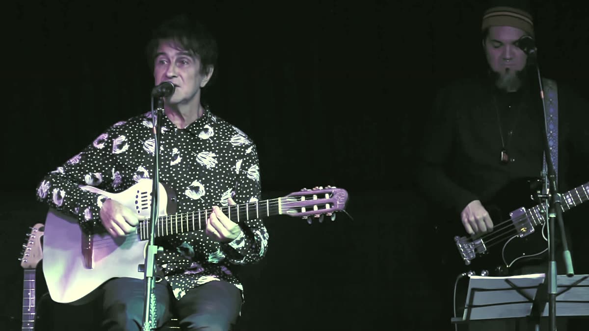 Gui Tavares singing and playing nylon string guitar on stage with a bass player behind him
